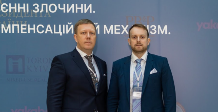 Two men in suits standing in front of a wall
Description automatically generated