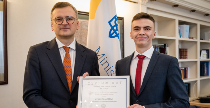 A person in suit and tie holding a certificate
Description automatically generated
